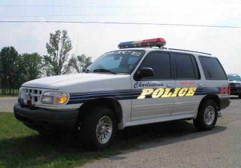 1998 Ford Crown Victoria - A white police SUV, likely a Ford Explorer, is parked on a grassy area with another vehicle visible in the background.