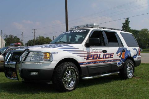 1998 Ford Crown Victoria - A white police SUV is parked on grass under a partly cloudy sky.