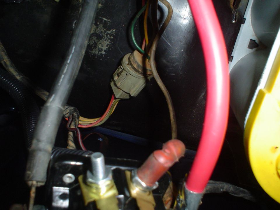 Close-up of a vehicle's wiring harness with red and black cables, a gray connector, and some electrical tape
