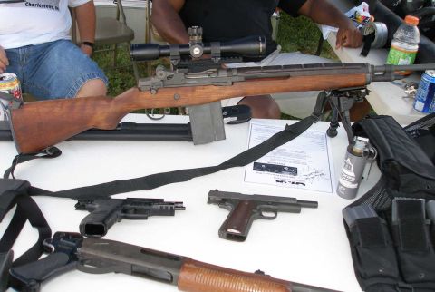 1998 Ford Crown Victoria - Various firearms and tactical gear are displayed on a table, possibly at an outdoor event.