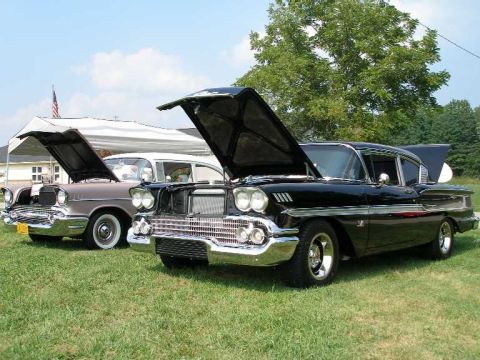 1998 Ford Crown Victoria - Two classic Chevrolet models, a 1958 Impala and a 1957 Bel Air, displayed at an outdoor car show.