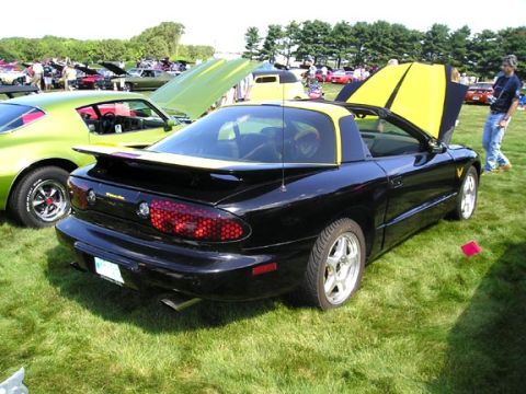 1984 Pontiac Fiero - A black 1994 Pontiac Trans Am with yellow accents is displayed at an outdoor car event.