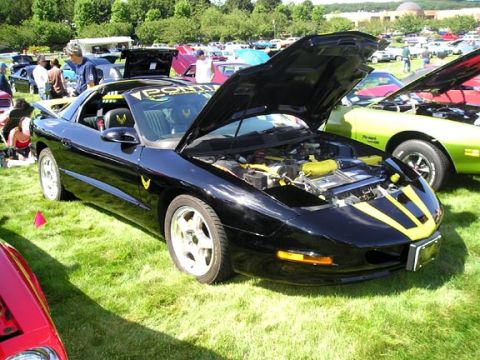 1984 Pontiac Fiero - Black 1994 Pontiac Firebird Trans Am with hood open, parked on grass at a car show.