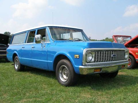 1998 Ford Crown Victoria - A blue Chevrolet Suburban is parked on a grassy field under a partly cloudy sky.