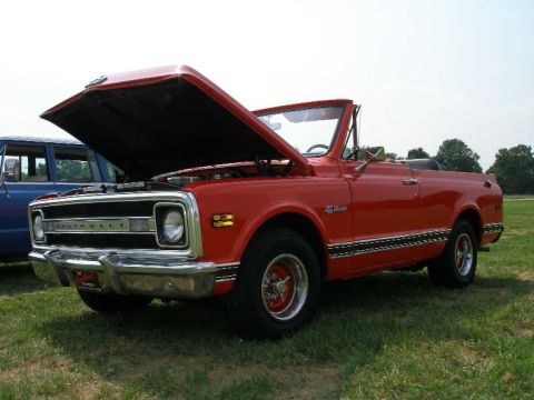 1998 Ford Crown Victoria - A red Chevrolet pickup truck with its hood open sits on a grassy field next to a blue SUV.