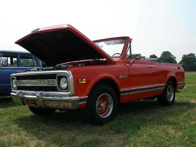 Red classic Chevrolet convertible with open hood parked on grass