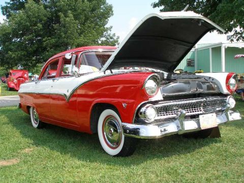 1998 Ford Crown Victoria - A classic red and white 1955 Ford Fairlane sedan is displayed with its hood open at an outdoor car show.