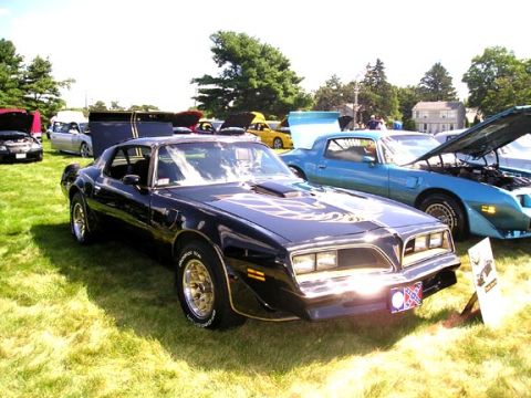 1984 Pontiac Fiero - Two Pontiac Trans Ams are parked on a grassy field at an outdoor car show.
