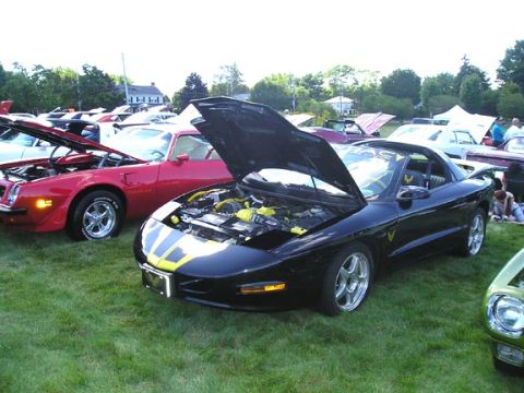 1984 Pontiac Fiero - A black Pontiac Firebird Trans Am is displayed with its hood open, yellow engine accents at an outdoor car event.