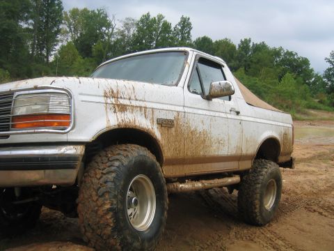 1996 Ford Bronco - Muddy 1996 Ford Bronco with off-road modifications sits on a dirt path after driving through mud.