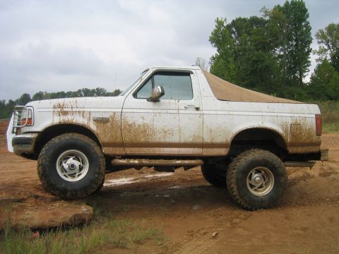 1996 Ford Bronco - This lifted SUV is shown off-road, covered in mud, with a tan soft top covering the rear.