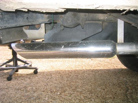 1996 Ford Bronco - Underbody shot of a polished stainless muffler and tailpipe mounted along the frame rail of a truck, propped on a stool during installation…