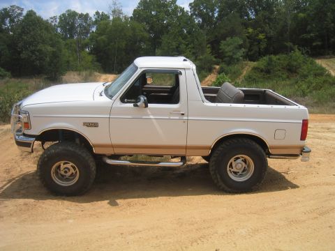 1996 Ford Bronco - Side view of a white 1996 Ford Bronco with lifted suspension on a dirt road.