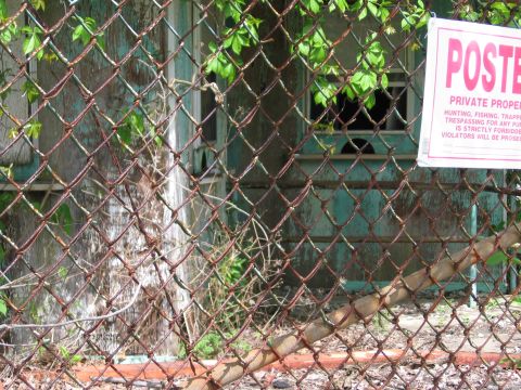 1997 Ford Probe - A rusty fence obscures an old, overgrown building. A sign warns against trespassing.