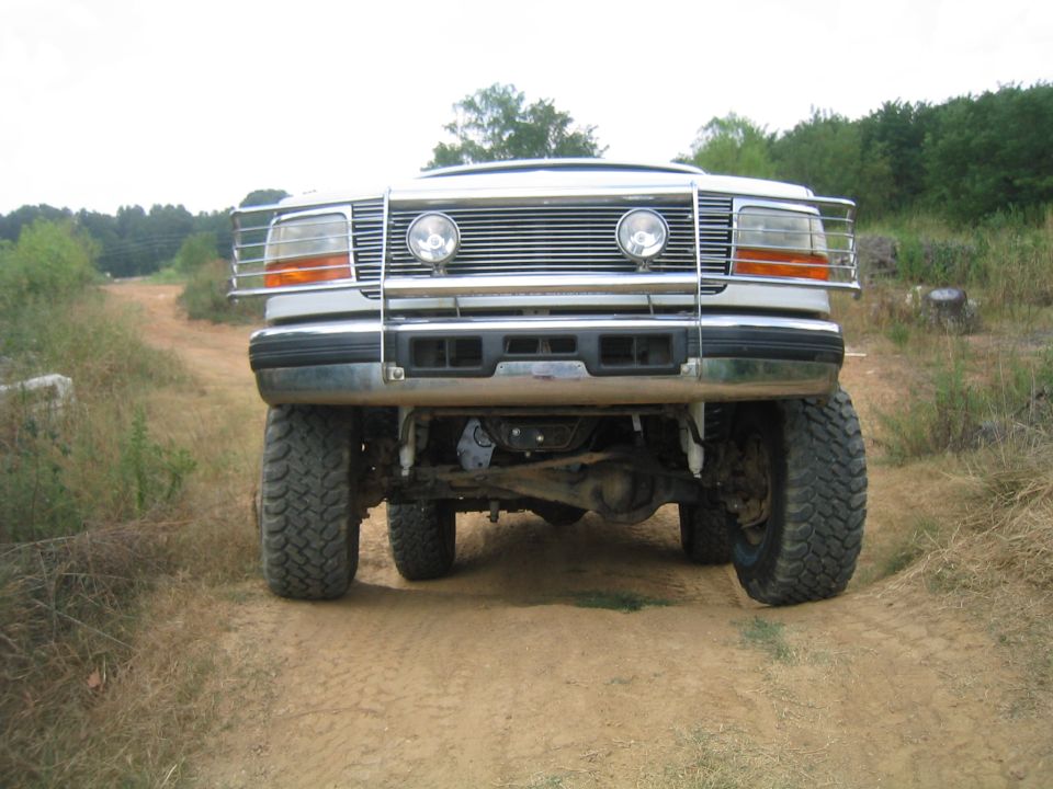 White Ford Bronco with a chrome grille guard and large tires on a dirt road