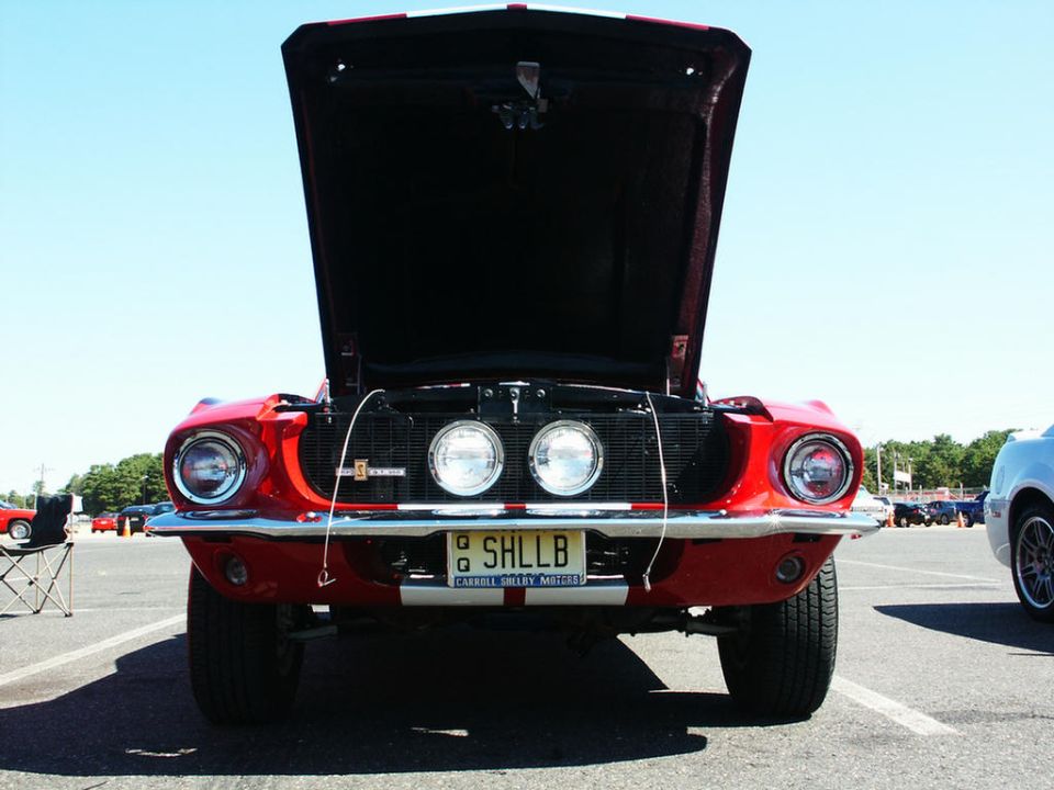 Front view of a red classic car with hood open. License plate reads SHLLB