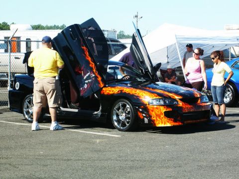 2001 Mercury Grand Marquis - A customized car with flame graphics and gullwing doors is displayed at a car show.