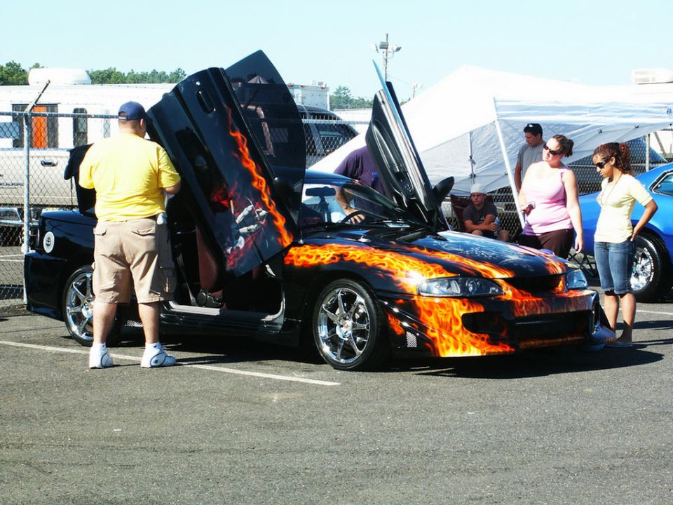 Black car with flame graphics and gullwing doors open, front view