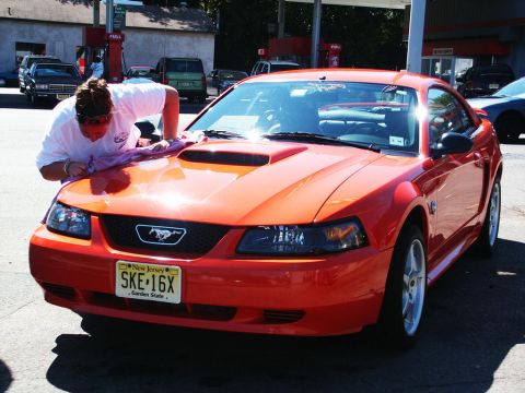 2001 Mercury Grand Marquis - Orange Ford Mustang with a hood scoop is being detailed at a gas station.