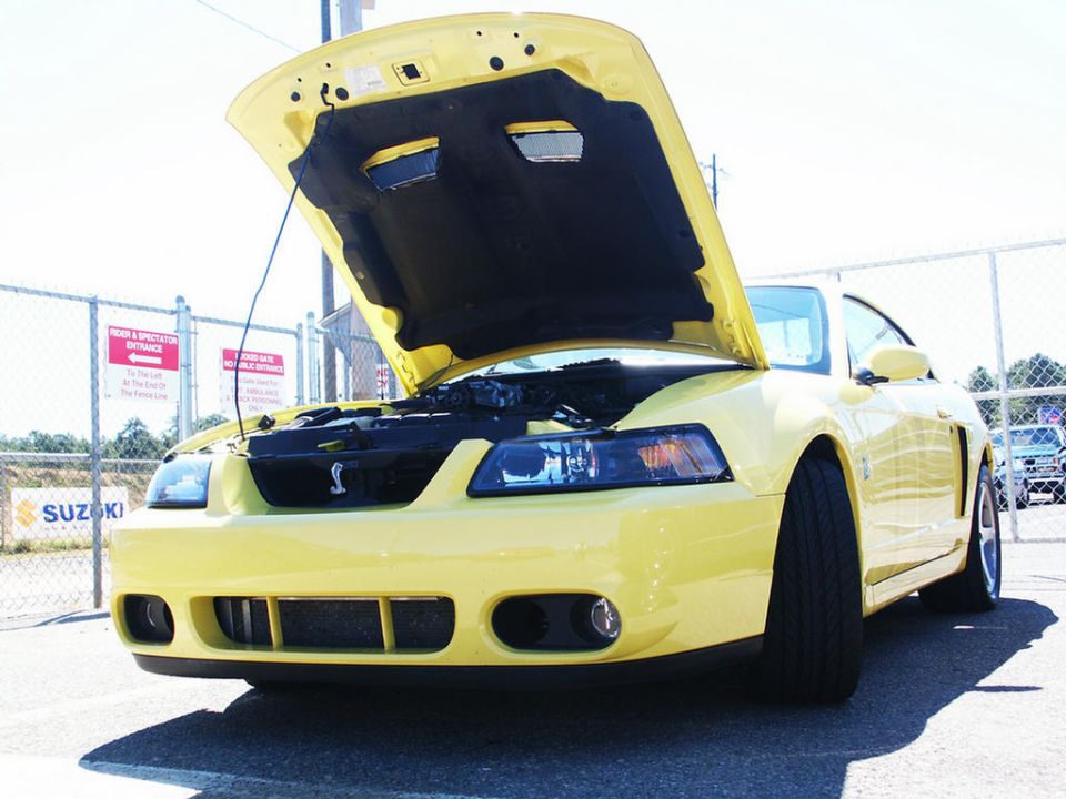 Yellow Ford Mustang Cobra with hood open, showing engine. Has a Cobra emblem on the grille