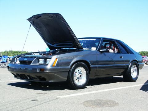 2001 Mercury Grand Marquis - A gray Ford Mustang is parked with its hood up at a car show under a clear blue sky.