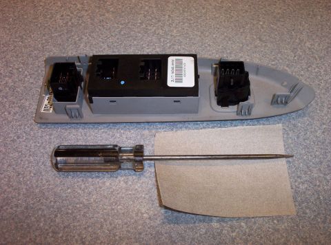 1998 Ford Crown Victoria - A car window switch assembly is shown with a screwdriver and a piece of paper.