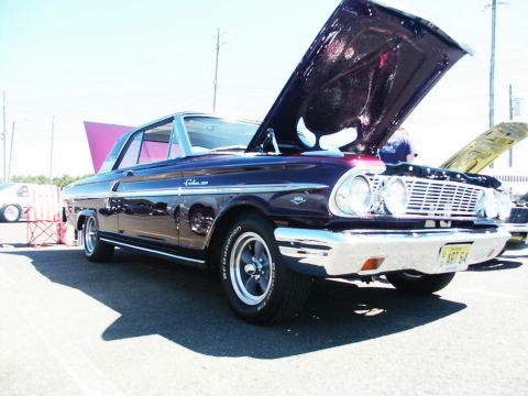 2001 Mercury Grand Marquis - A purple 1964 Ford Falcon 2-door coupe is displayed with its hood open at a car show.