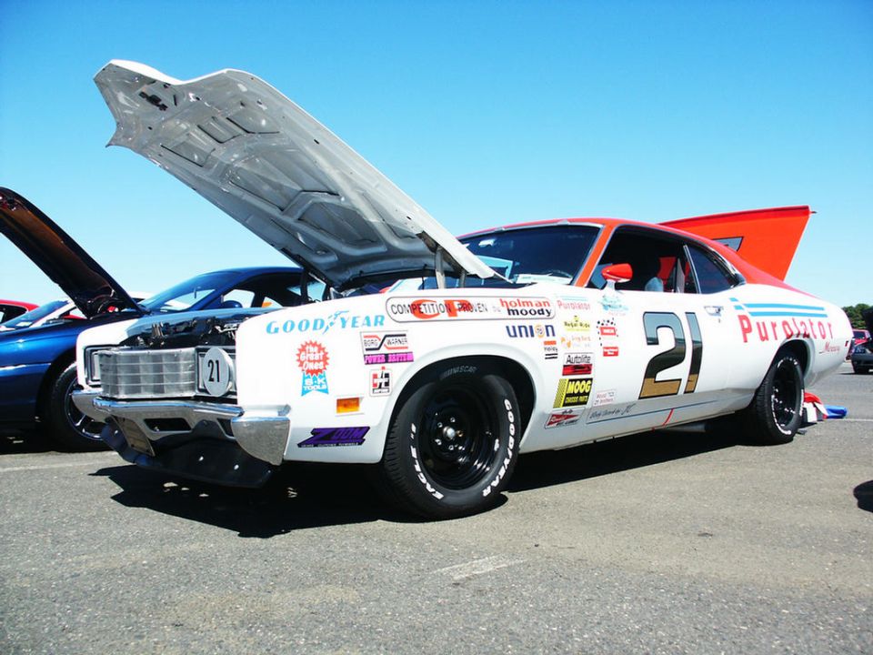 Race car with hood open, number 21, Goodyear tires, and various sponsor decals. Another car is visible to the left