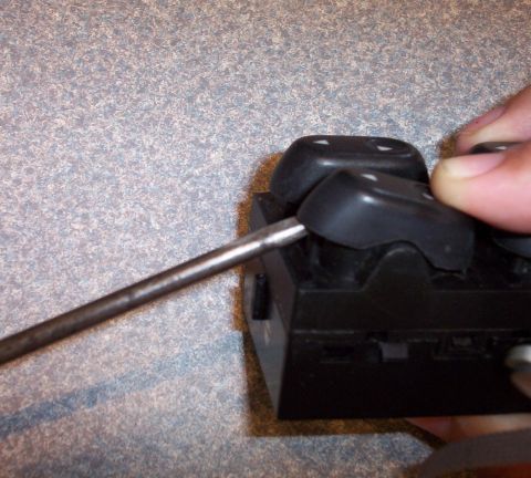 1998 Ford Crown Victoria - A screwdriver is used to pry a button on a vehicle's window switch assembly.