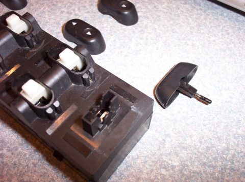 1998 Ford Crown Victoria - A disassembled window switch assembly is shown, with one button detached from the main unit.