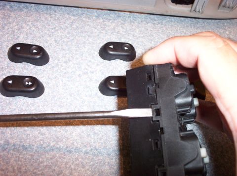 1998 Ford Crown Victoria - A screwdriver is used to remove a car's window control switch assembly, with several detached buttons visible.