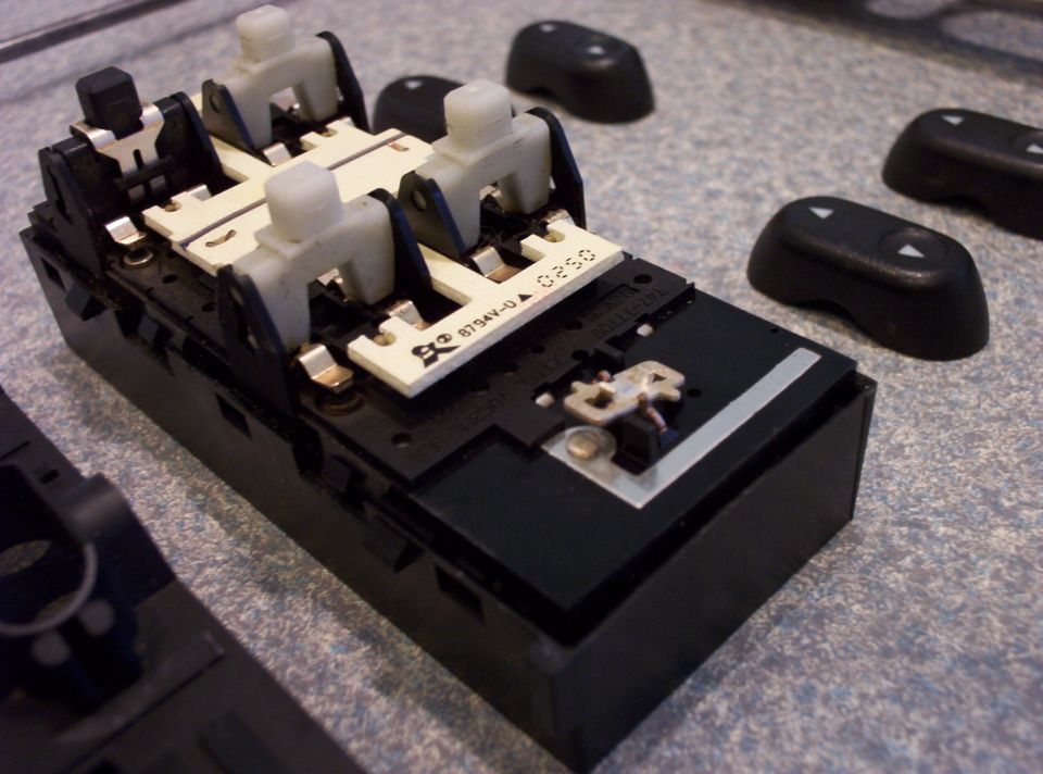 Power window switch assembly with four white actuators and circuit board, separate black button caps nearby