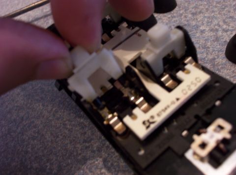 1998 Ford Crown Victoria - A person's fingers are shown adjusting white plastic clips on a circuit board with visible electronic components and markings.