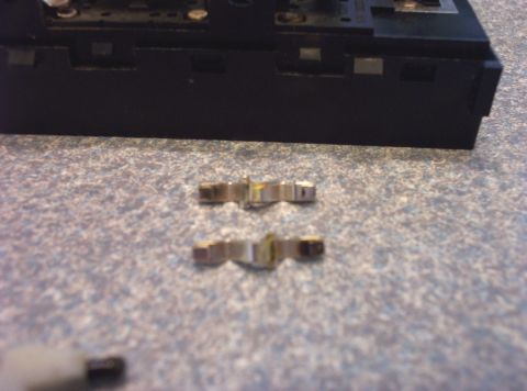 1998 Ford Crown Victoria - Close-up of two metal clips and a black electronic component on a speckled surface.