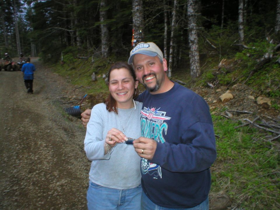 Two people posing on a gravel forest trail with ATVs in the background