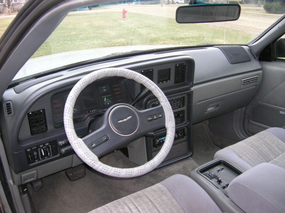 Car interior showing dashboard, steering wheel with white cover, and seats. A fire hydrant is visible through the windshield