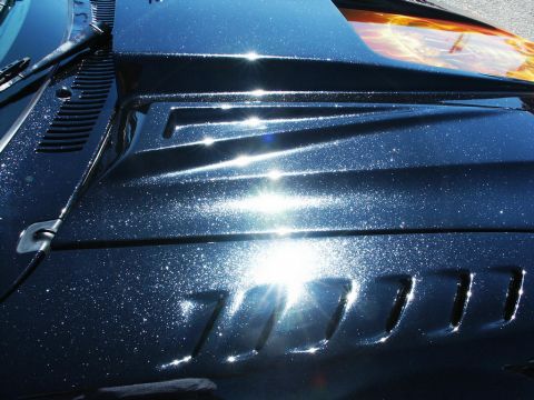 2001 Mercury Grand Marquis - The hood of a car features a metallic paint job with flame graphics and sculpted vents, reflecting bright sunlight.