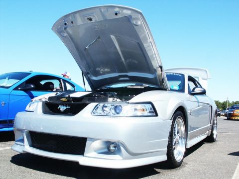 2001 Mercury Grand Marquis - A silver 2001 Ford Mustang is displayed with its hood open at a car show, with another blue car visible to the left.