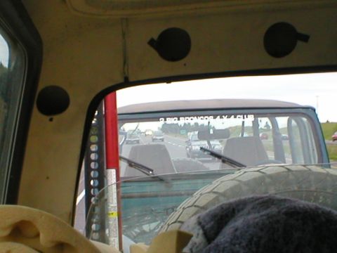 1978 Ford Bronco - View from inside a vehicle, looking out the rear window at other vehicles on the road. A spare tire is visible in the foreground.