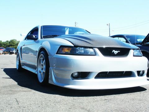 2001 Mercury Grand Marquis - A silver Ford Mustang with a carbon fiber hood is parked at a car show, with other vehicles in the background.