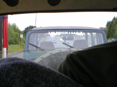 1978 Ford Bronco - View from inside a 1978 Ford Bronco, showing the rear window and highway traffic. A club decal is visible on the glass.