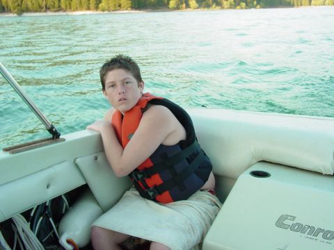 1986 Ford Bronco - A young person wearing a life jacket is on a boat ride with a wooded shoreline visible.