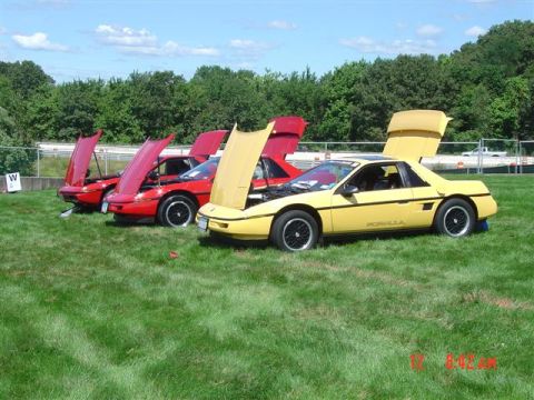 1984 Pontiac Fiero - Three Pontiac Fieros displayed with hoods and rear decks open on a grassy field.