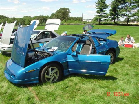 1984 Pontiac Fiero - A blue 1984 Pontiac Fiero is displayed with its doors and hood open, while other cars are visible in the background.