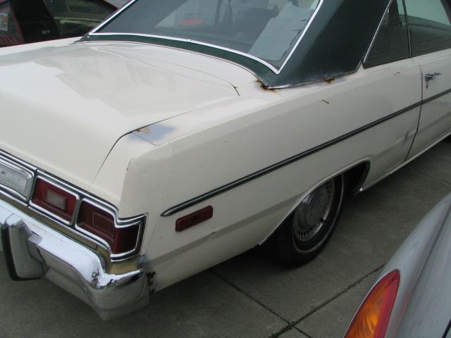 Rear quarter of a white sedan with a green vinyl top. Another car is partially visible in the foreground