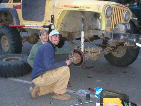 1978 Ford Bronco - Men performing maintenance on a Jeep CJ, possibly a Bronco enthusiast club event.