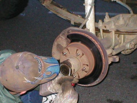 1978 Ford Bronco - A close-up view of a vehicle's brake rotor and hub assembly, with a person's gloved hand working on it.