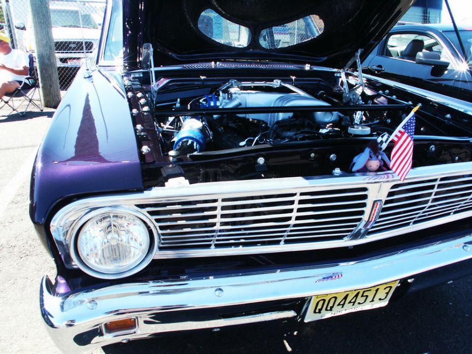 1964 Ford Falcon front grille and exposed engine bay, with an American flag and toy. Another car is visible behind