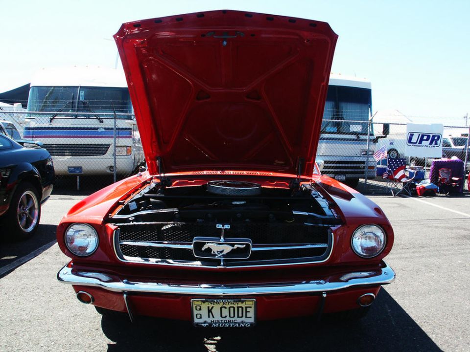 Red 1965 Ford Mustang front view, hood open, showing engine. License plate reads 'K CODE'