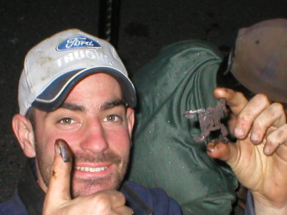 Man in a Ford Trucks cap with greasy hands grinning during a night wrenching session